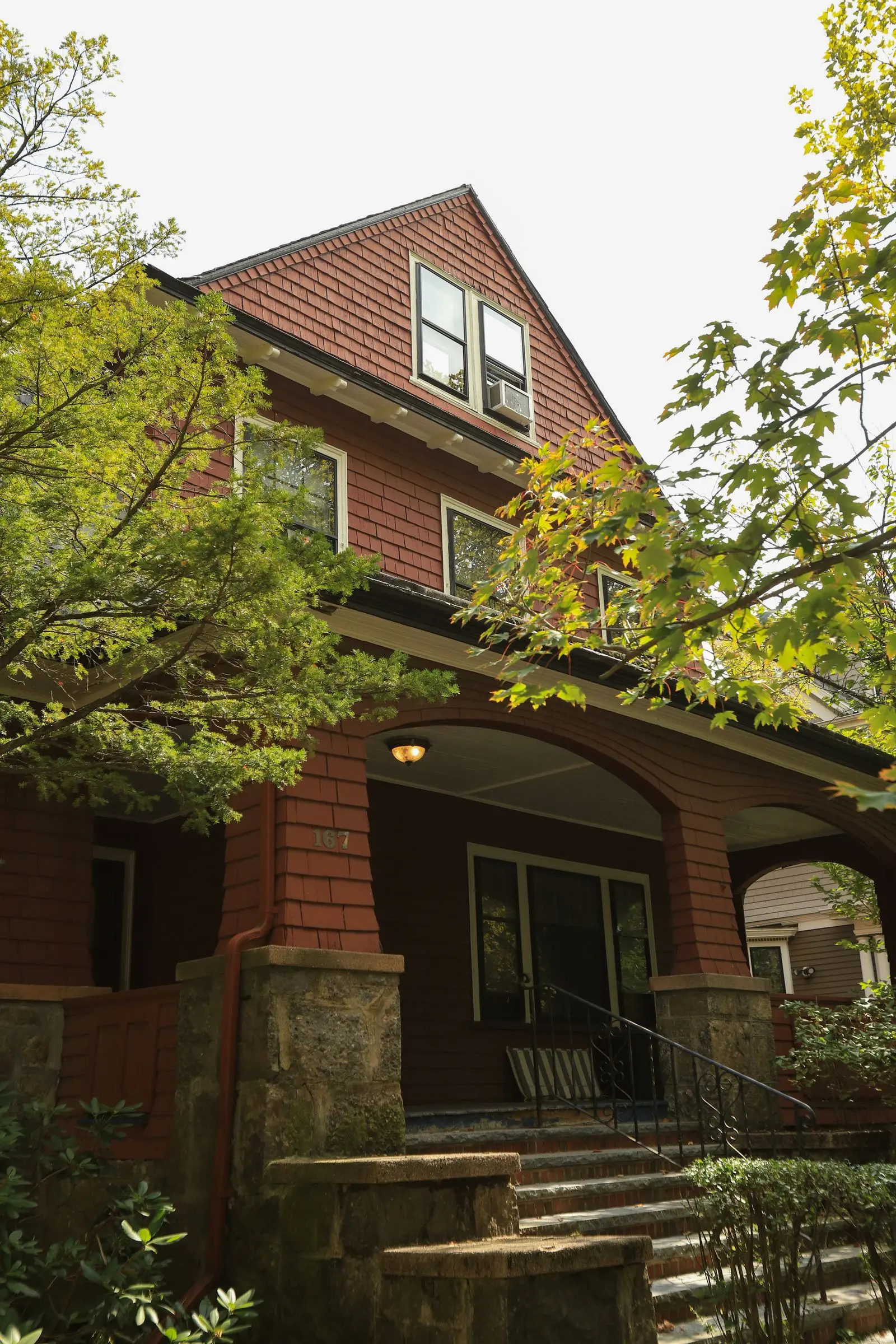 A brick craftsman-style house with a deep front porch under trees