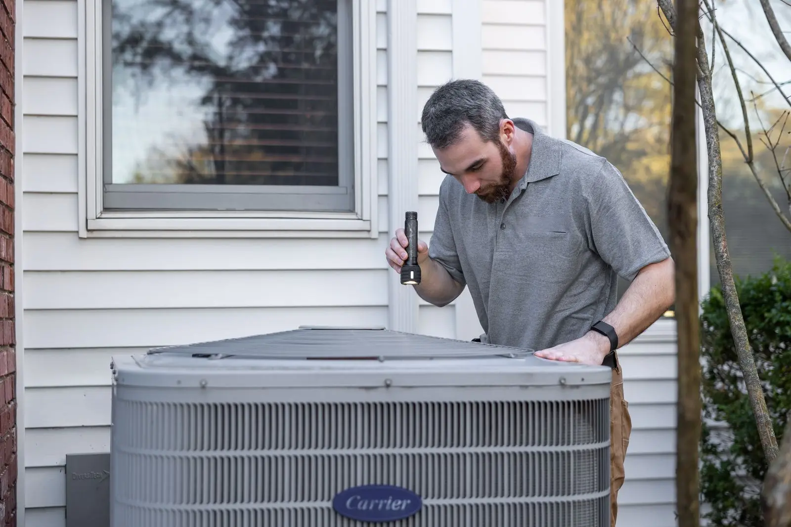 A technician checking an outdoor heat pump unit beside a house
